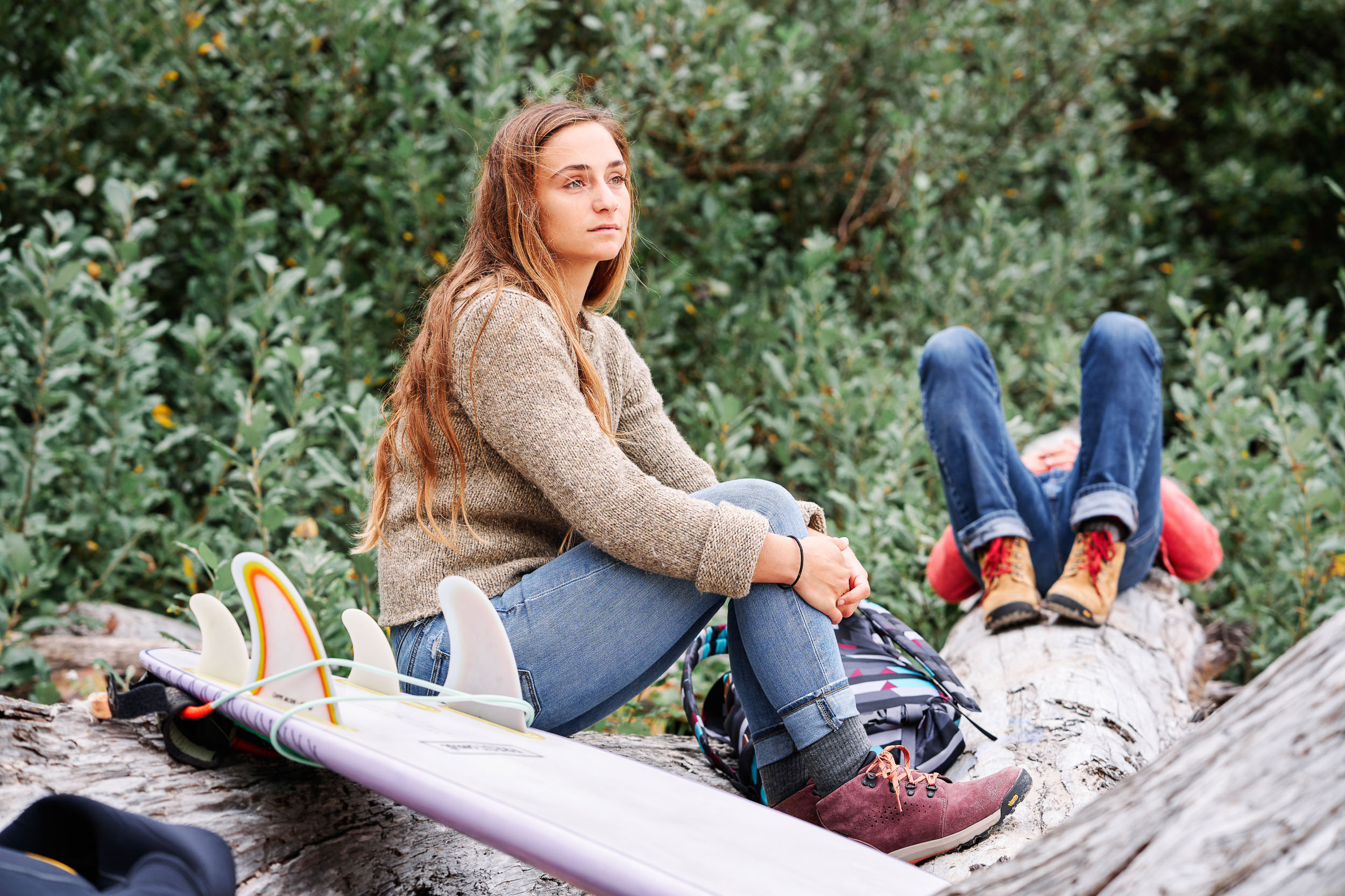 Surfer relaxing on logs at Cannon Beach while wearing Danner Inquires